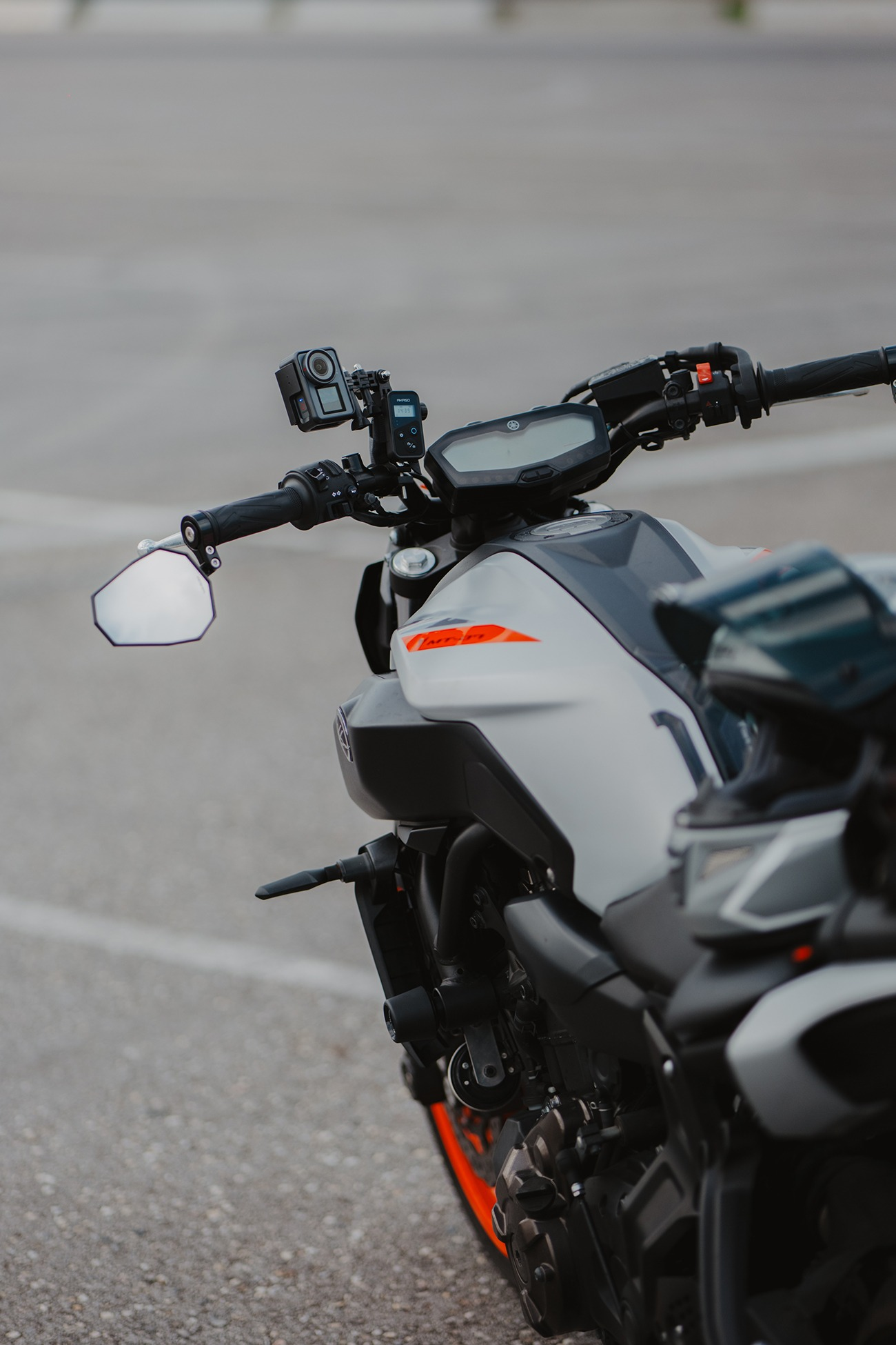Graues Motorrad mit Kamera und Spiegel auf dem Lenker, orange Akzente.