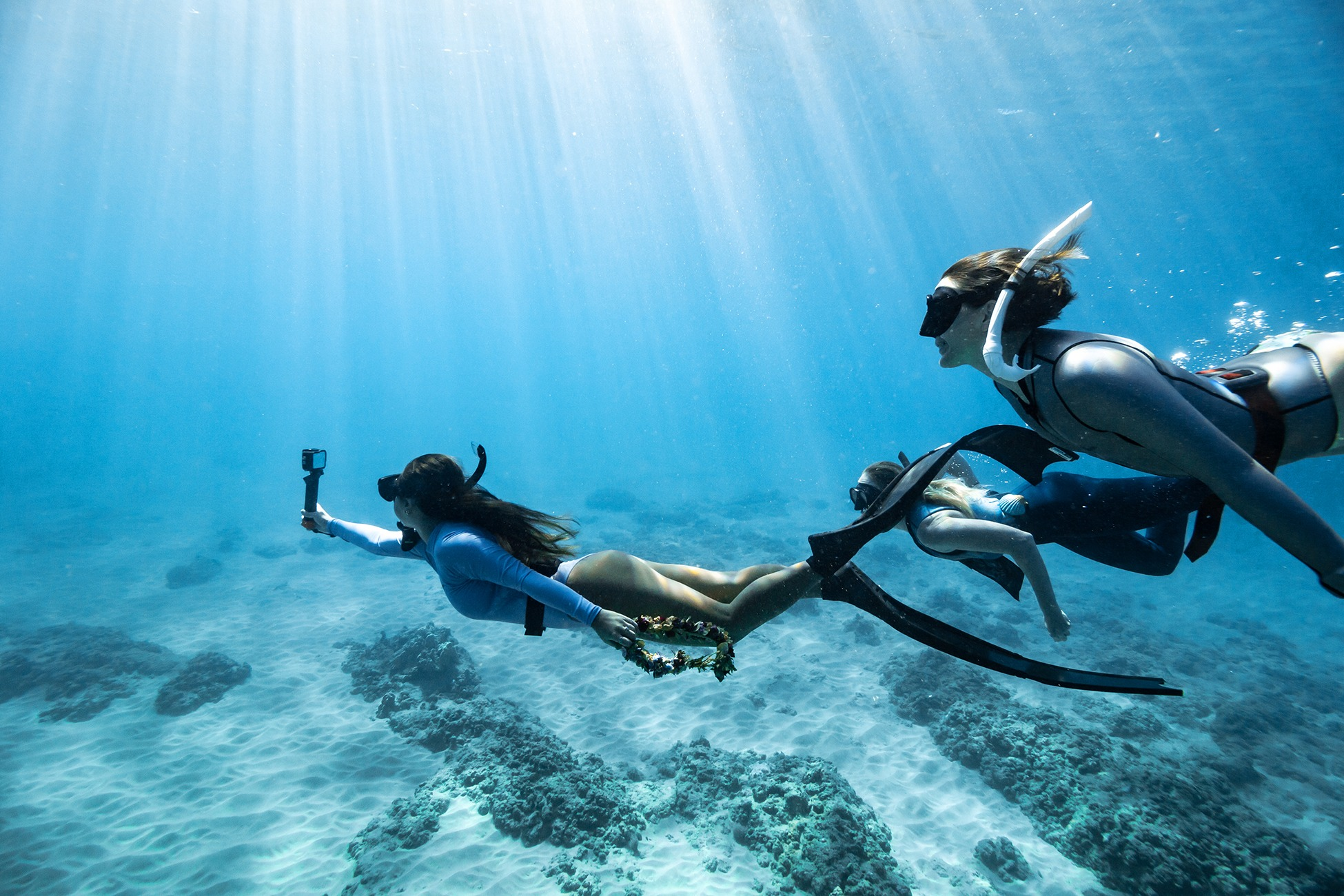 Drei Freitaucher schwimmen unter Wasser. Einer hält eine Kamera.