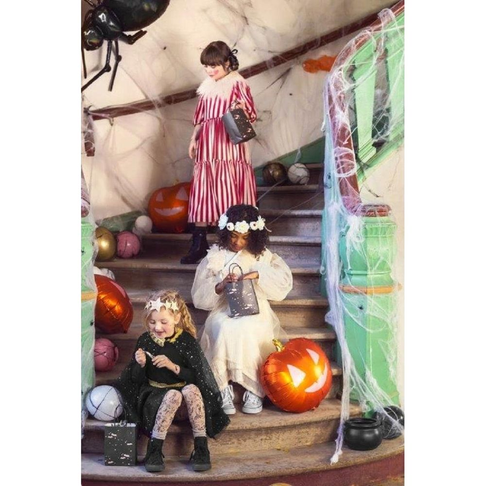 Drei Kinder in Kostümen auf einer Treppe mit Halloween-Dekorationen.