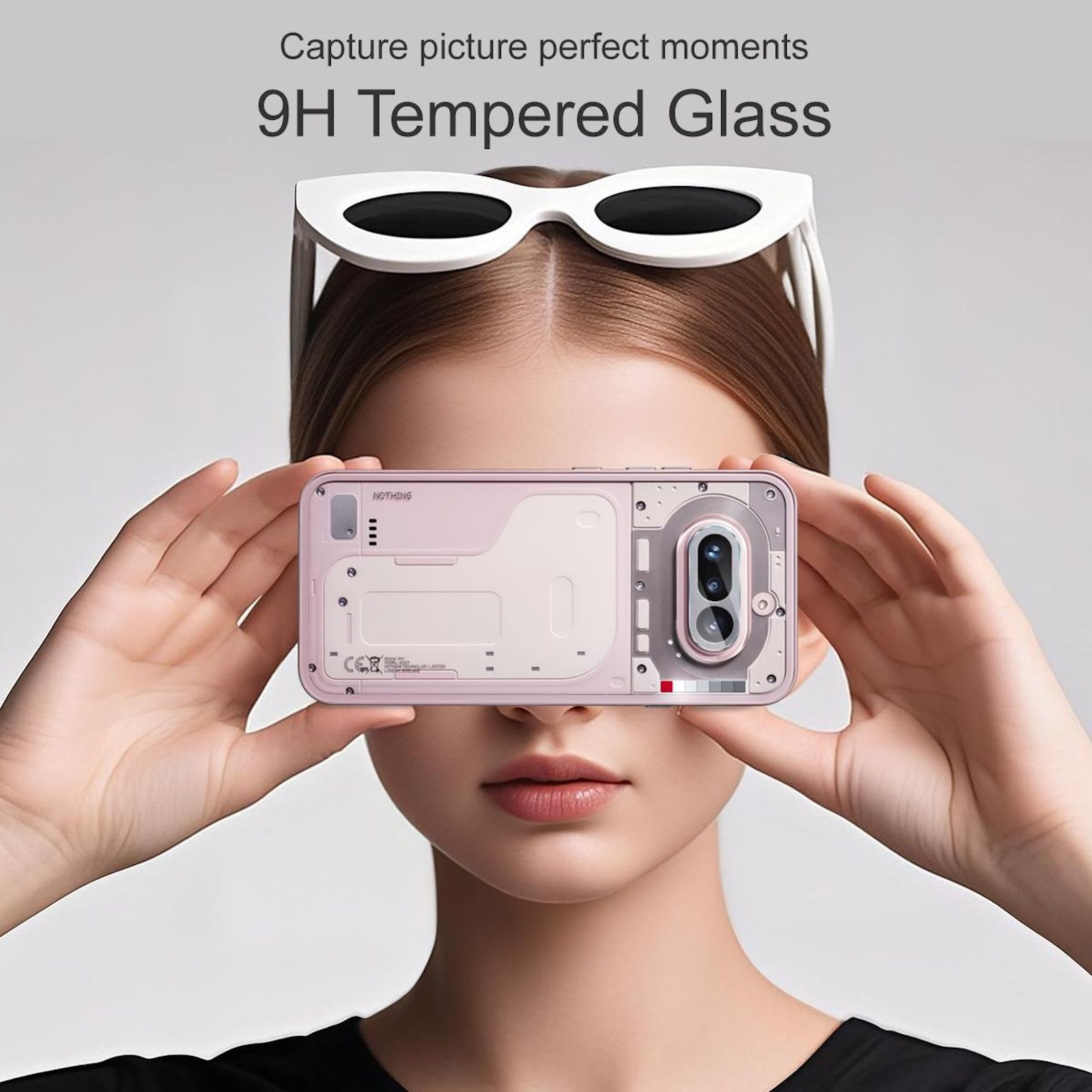 Una donna tiene in mano uno smartphone rosa con retro trasparente davanti al viso.