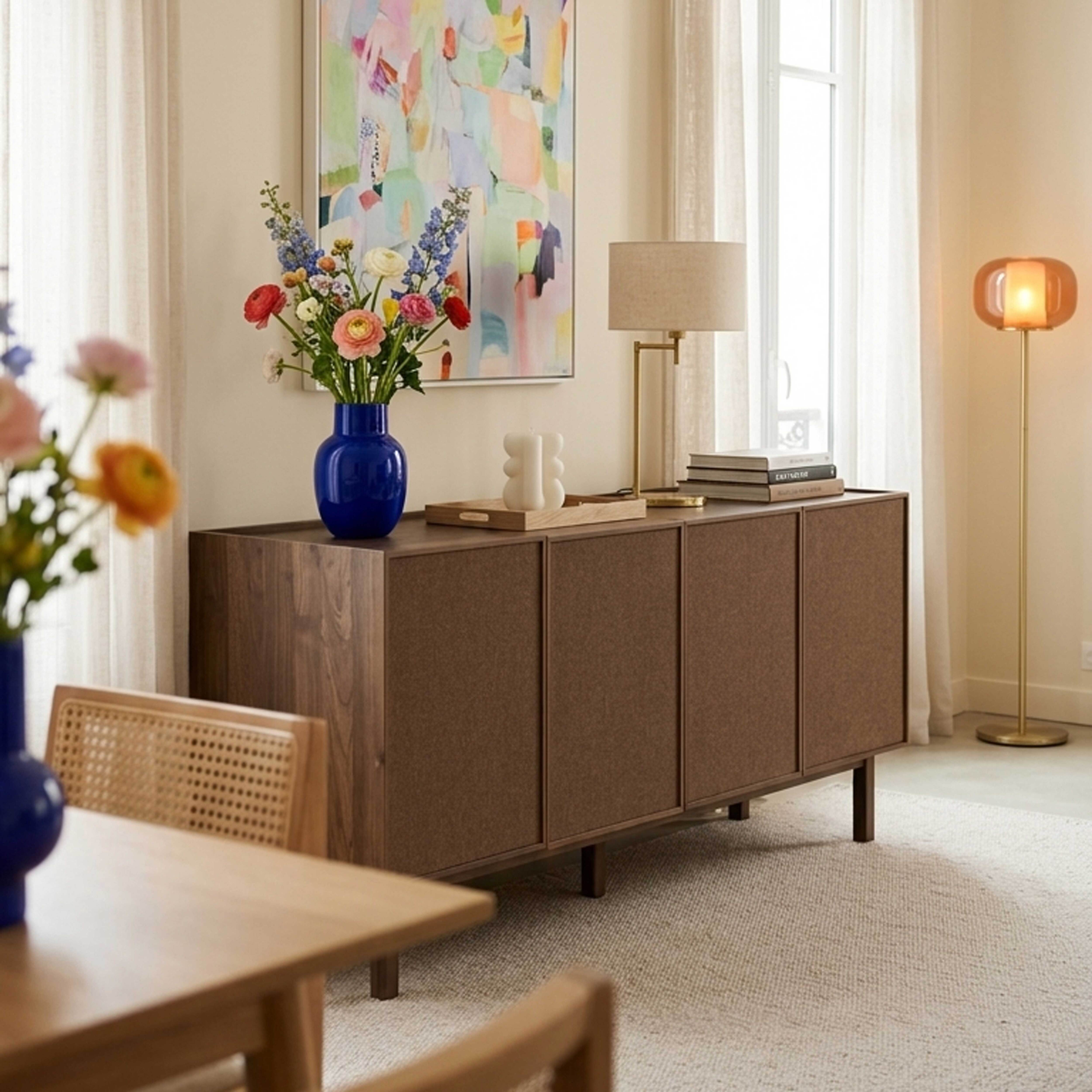 Ein braunes Sideboard mit Blumen und Lampe in einem hellen Raum.
