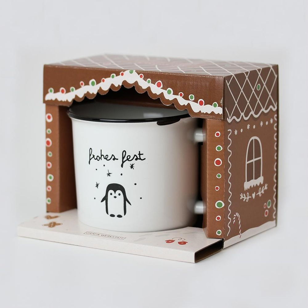 Eine weiße Tasse mit Pinguin-Motiv in einer Lebkuchenhaus-Verpackung.