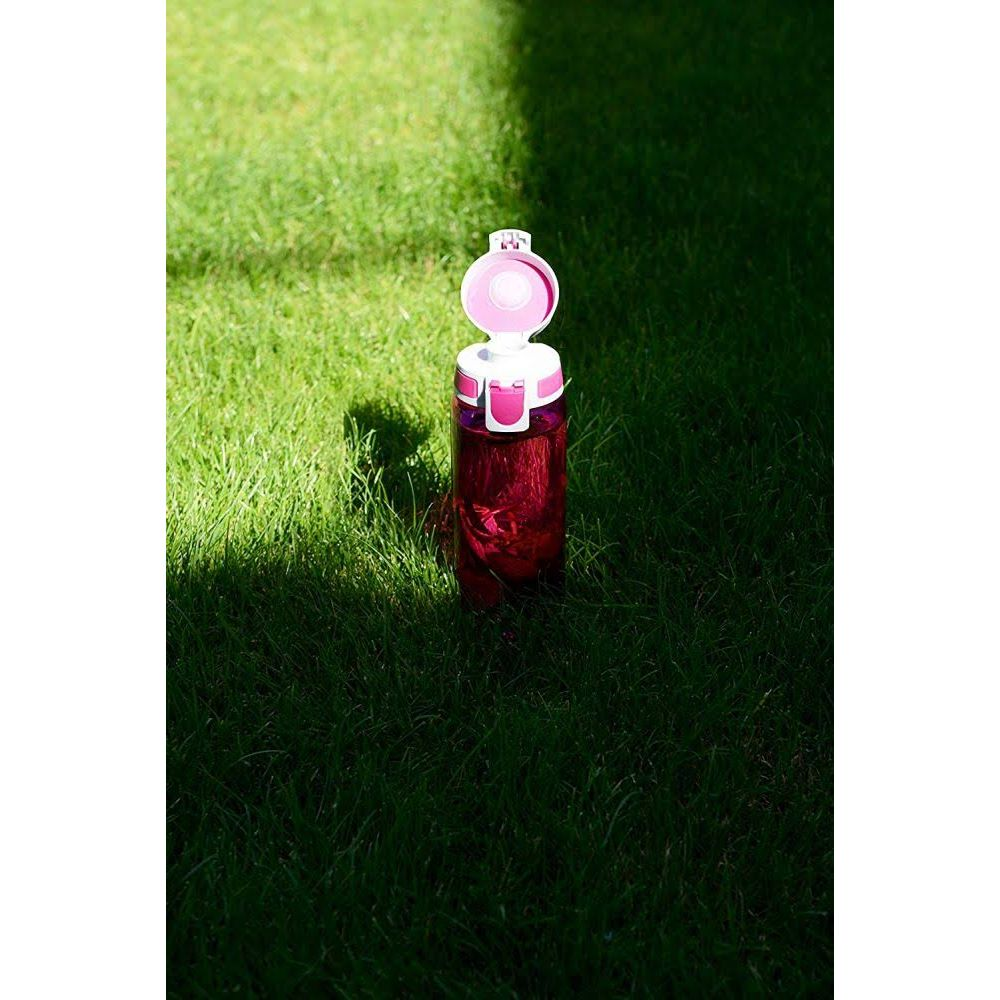 Eine pinke Wasserflasche mit weißem Deckel steht auf grünem Gras.