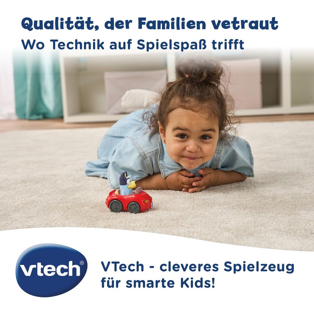 Ein lächelndes Kind liegt auf einem hellen Teppich und betrachtet ein rotes Spielzeugauto mit einer blauen Figur darin.