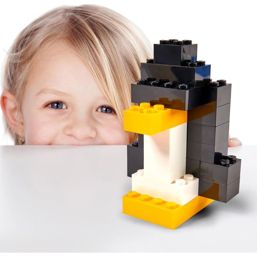 Un enfant jette un coup d'œil par-dessus une surface blanche sur un pingouin en briques noir, blanc et jaune.