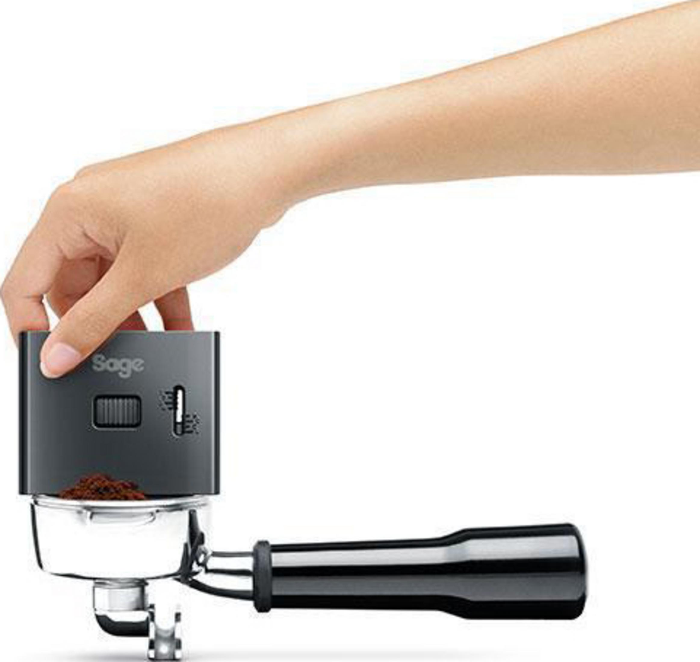 Una mano tiene un portafiltro con caffè macinato e un dispositivo Sage.