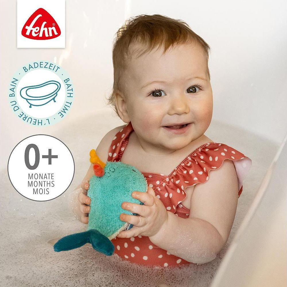 Ein Baby in einem roten Badeanzug mit Punkten hält ein türkisfarbenes Spielzeug in der Badewanne.