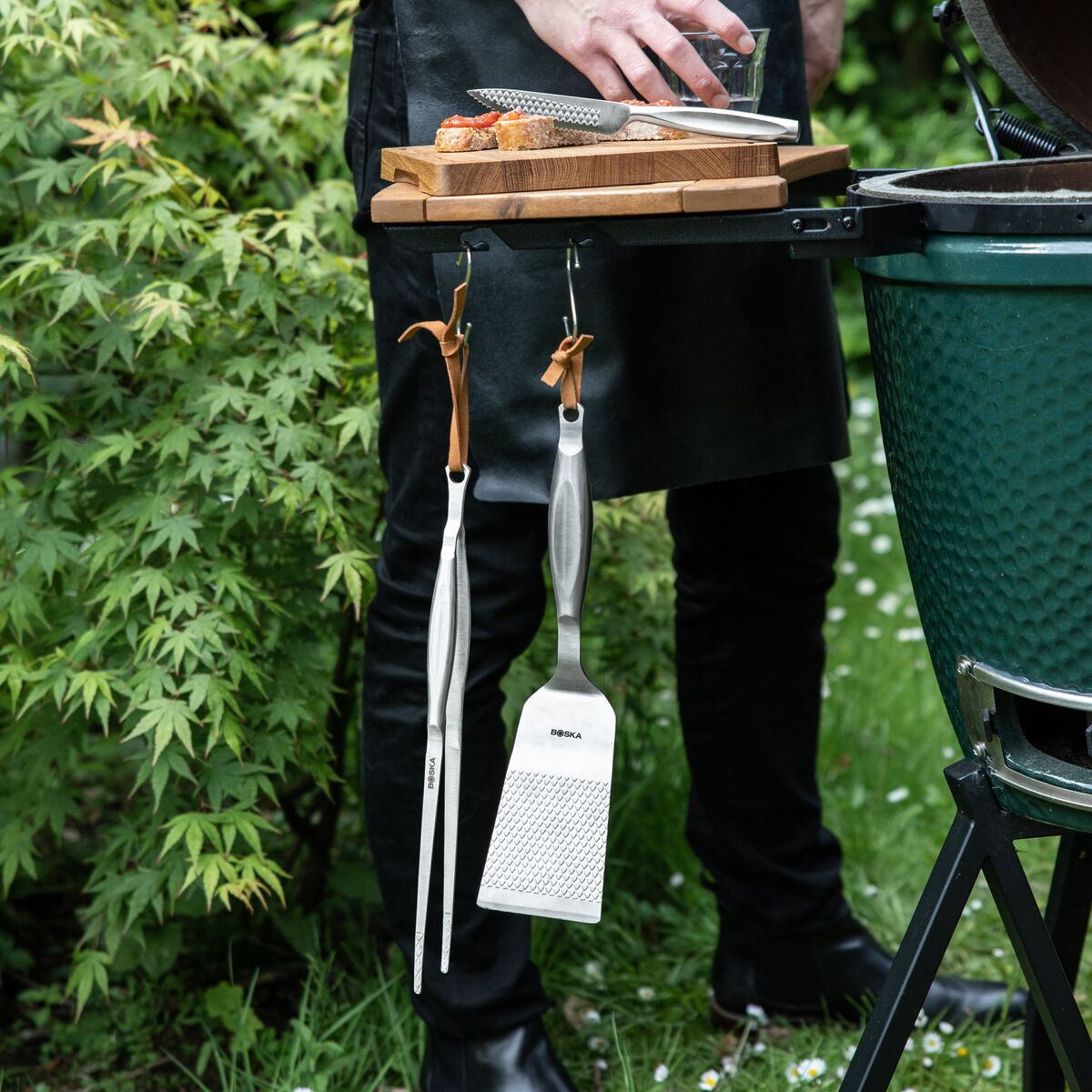 Attrezzi da barbecue appesi a una griglia nera. Persona prepara il cibo.