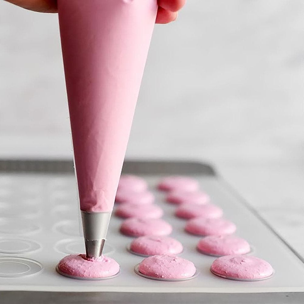Eine rosa Spritzbeutel-Tülle gibt rosa Teig auf eine Backmatte für Macarons.