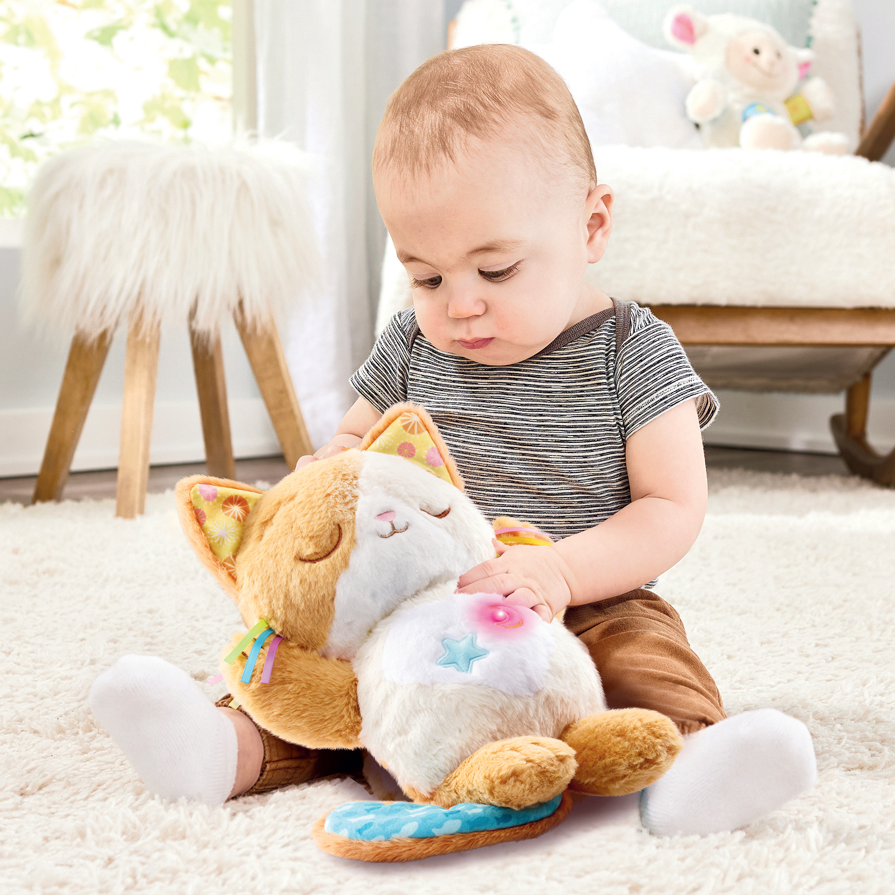Baby spielt mit einem weichen Spielzeugkätzchen, das auf einem Teppich sitzt.