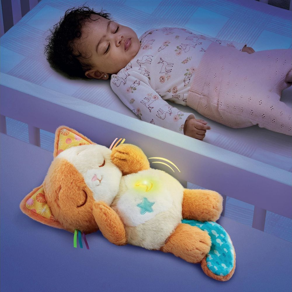 Ein Baby schläft in einem Bett neben einem leuchtenden Plüschtier in Katzenform.