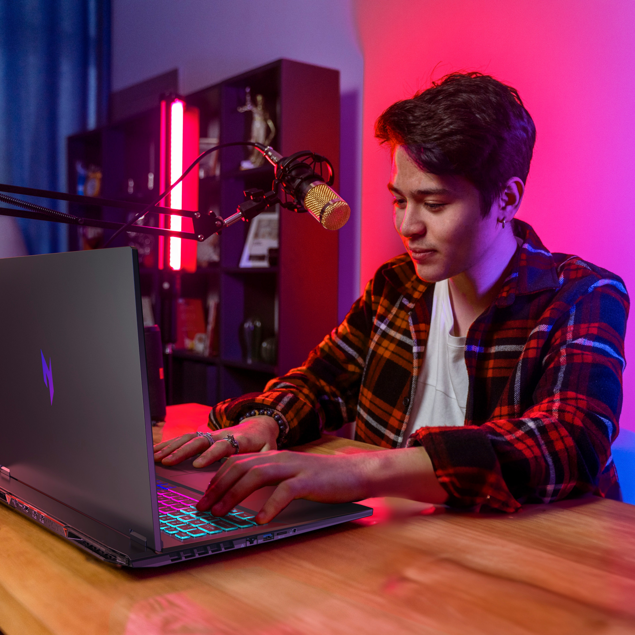 Ein Mann tippt auf einem Laptop mit beleuchteter Tastatur, Mikrofon daneben.