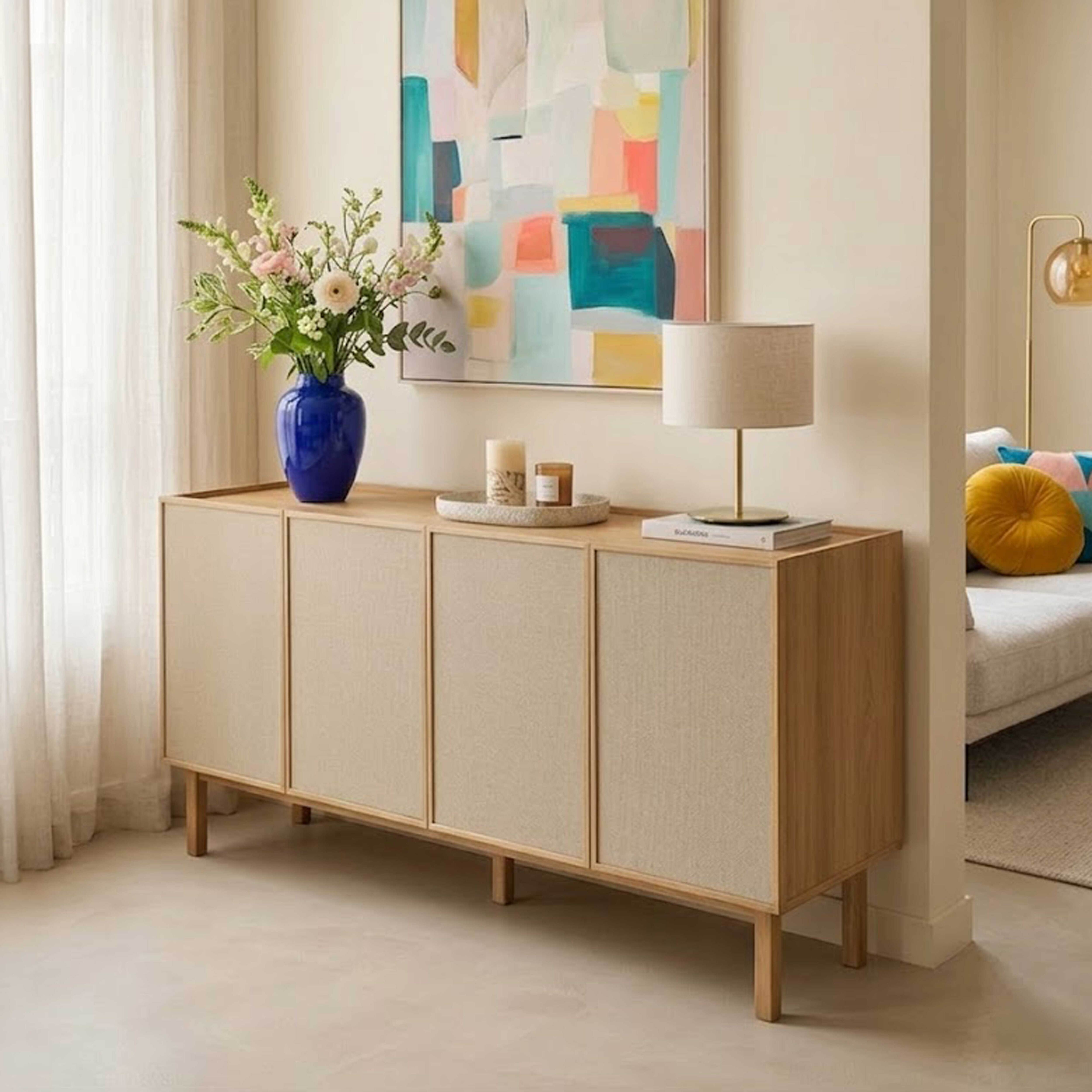 Ein helles Sideboard mit Stofffronten, geschmückt mit Blumen und Kerzen.