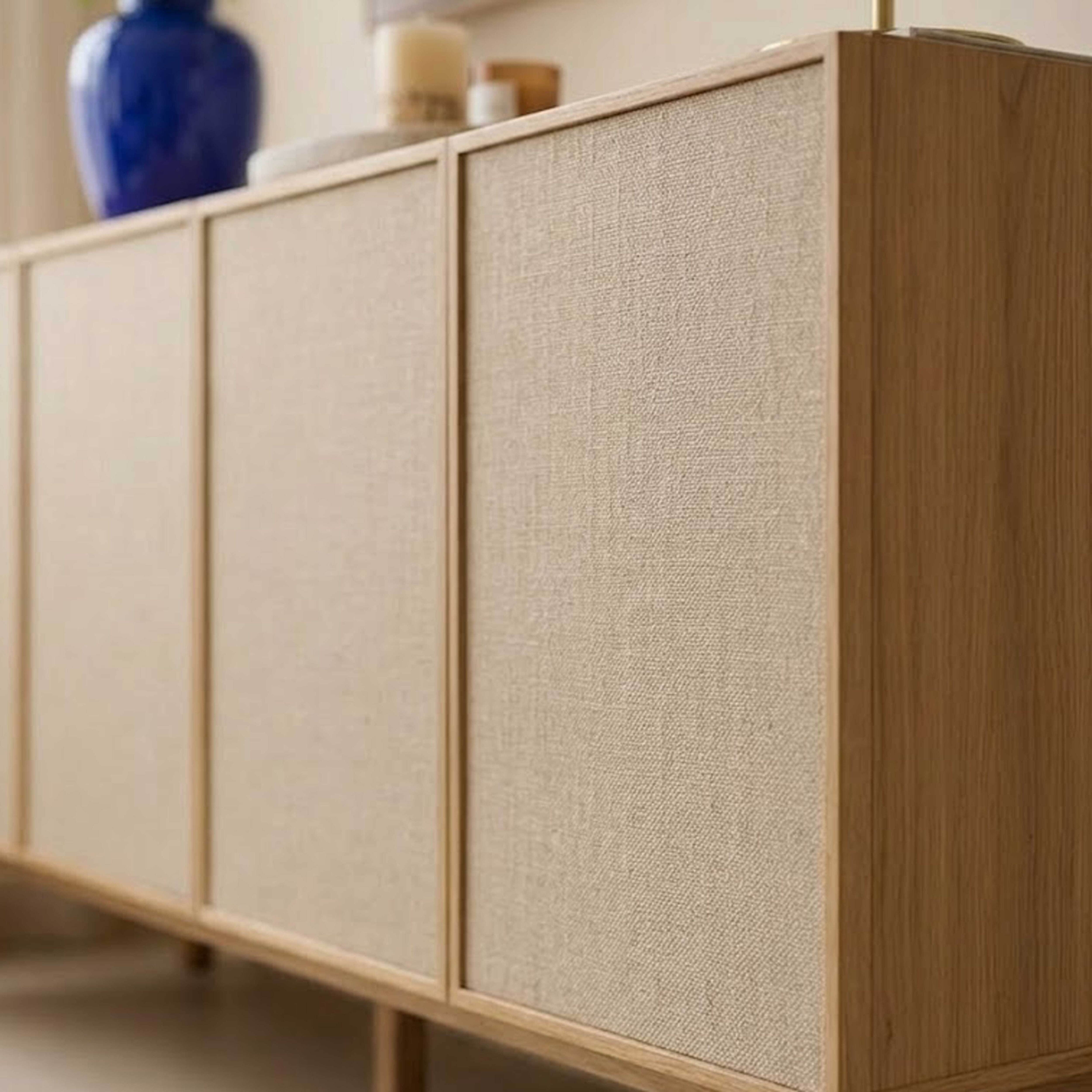 Ein hölzerner Schrank mit Stofffronten und einer blauen Vase darauf.