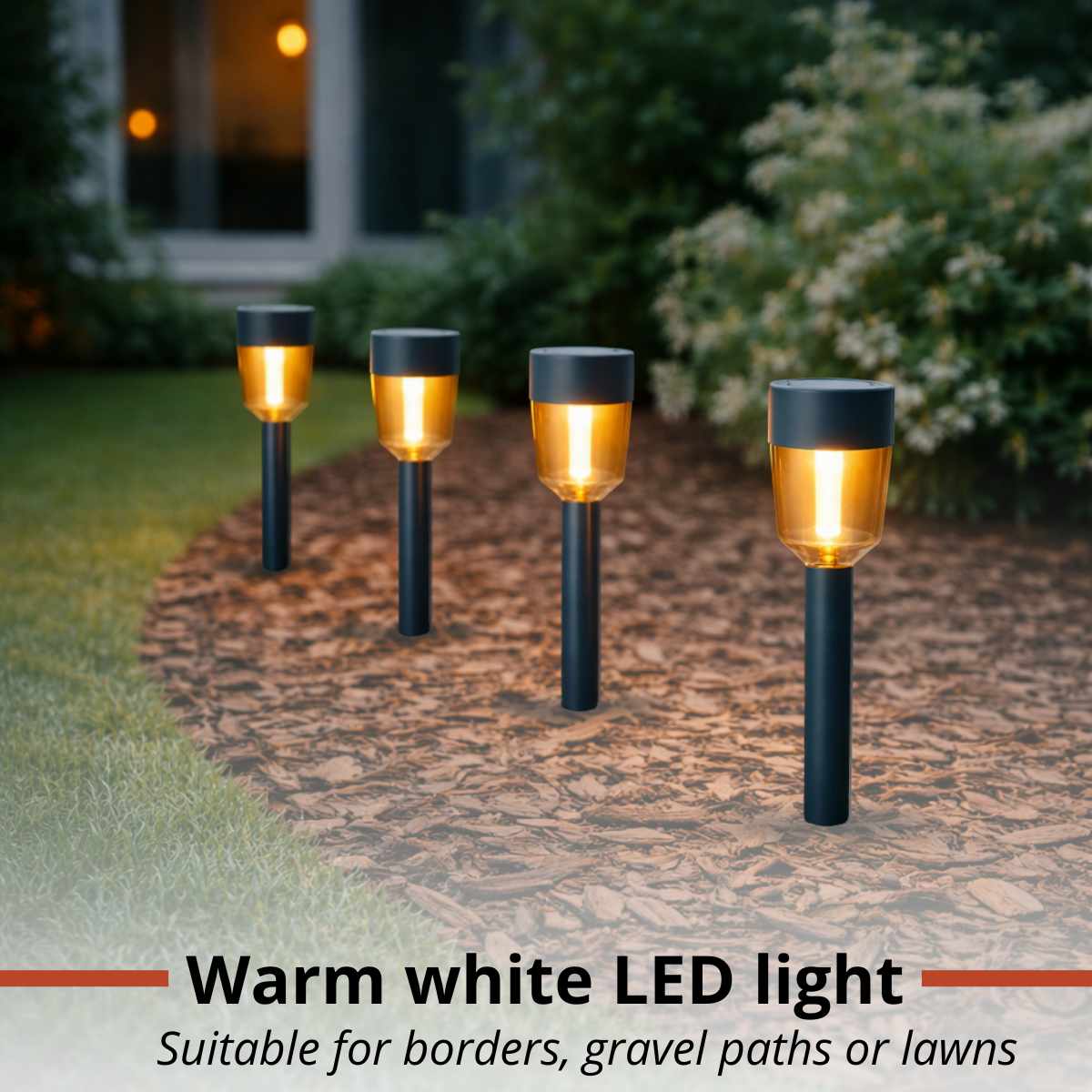 Four illuminated LED garden lights stand on a gravel path in front of a house.