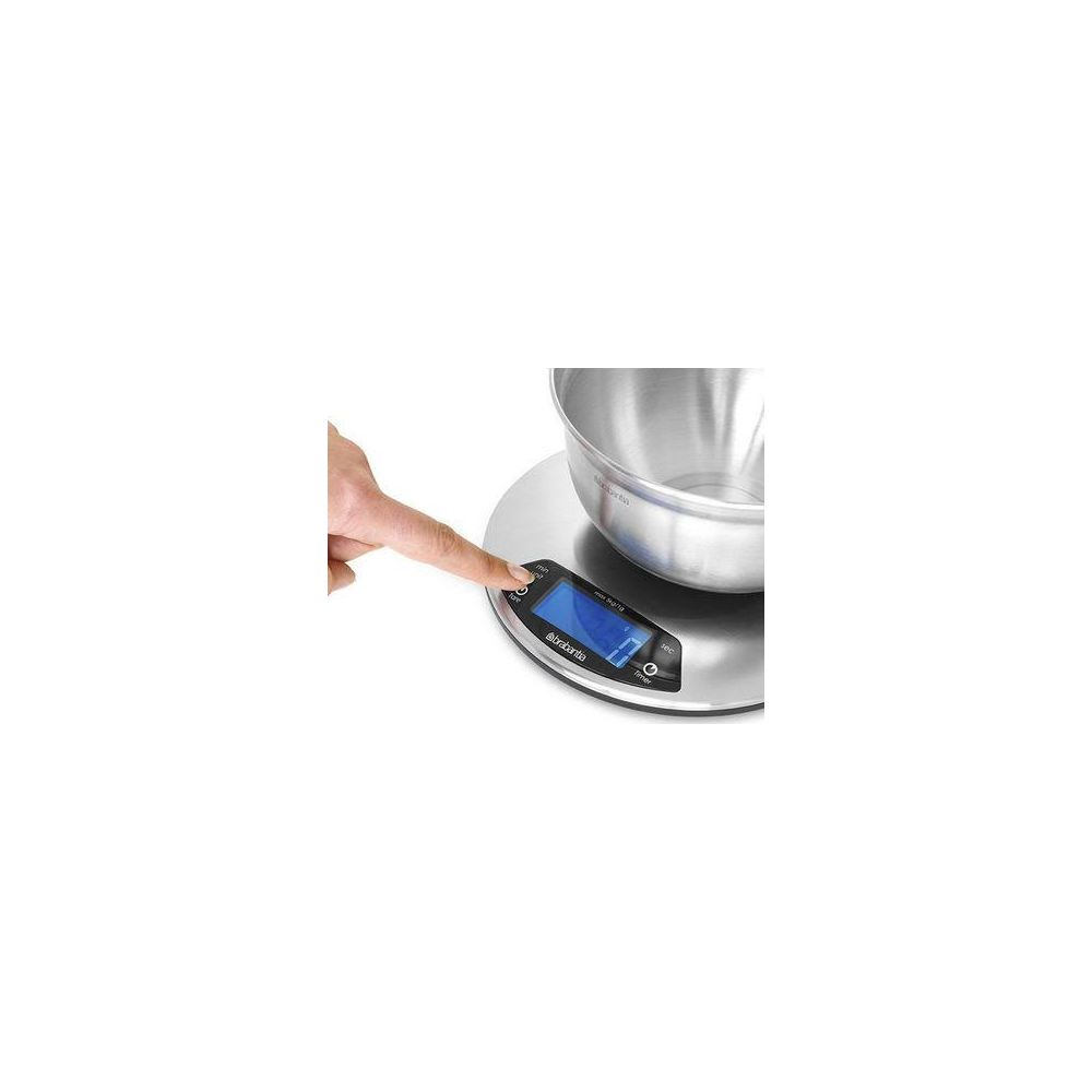 Una mano preme il pulsante 'tara' su una bilancia da cucina digitale con ciotola in acciaio.