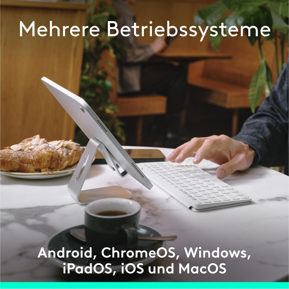 Tablet z klawiaturą, kawą i rogalikiem na marmurowym stole.