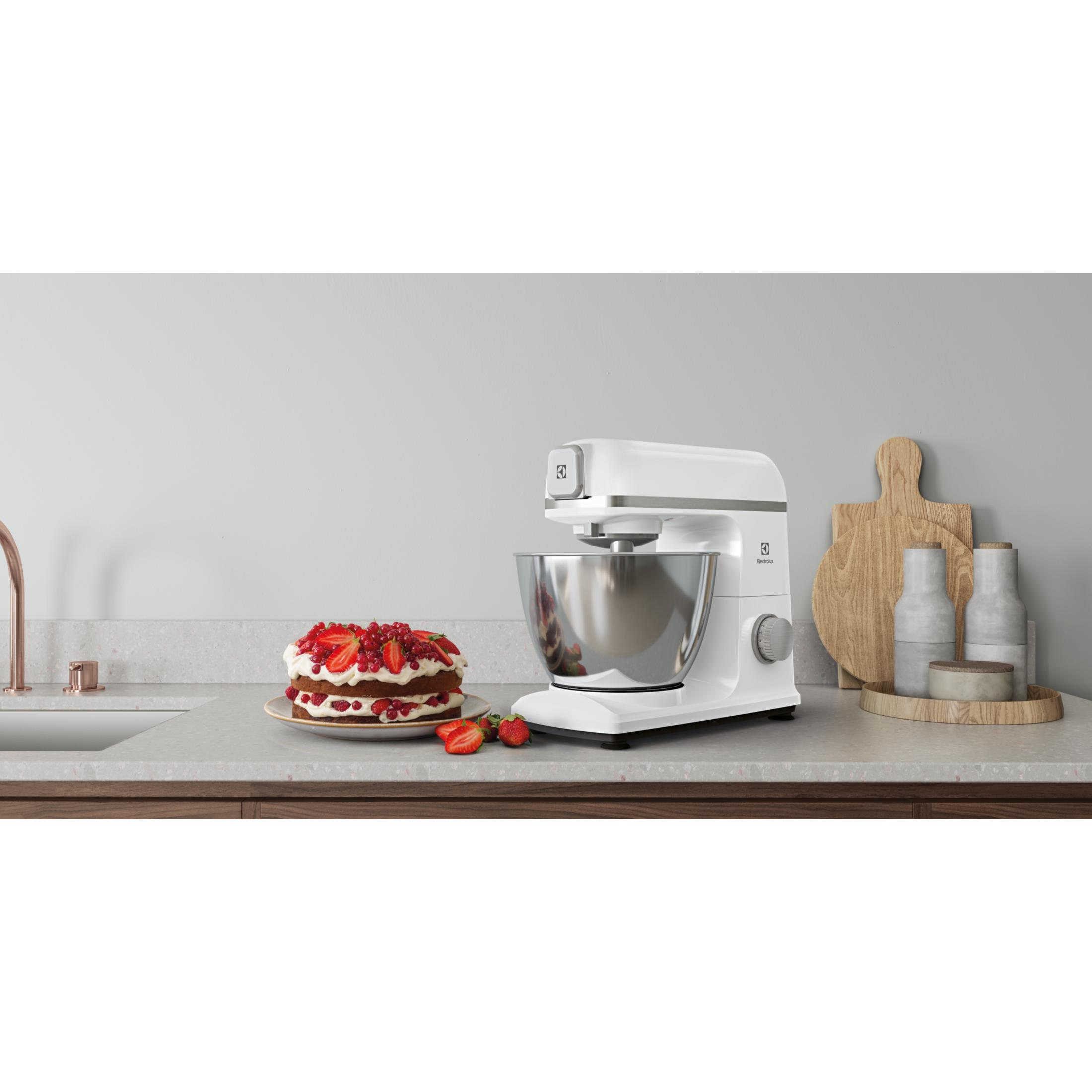 A white stand mixer next to a cake decorated with berries and cream.