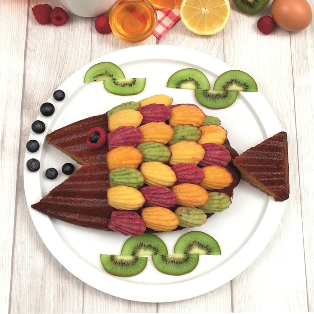 Fischkuchen mit bunten Madeleines, Kiwi und Blaubeeren auf einem Teller.