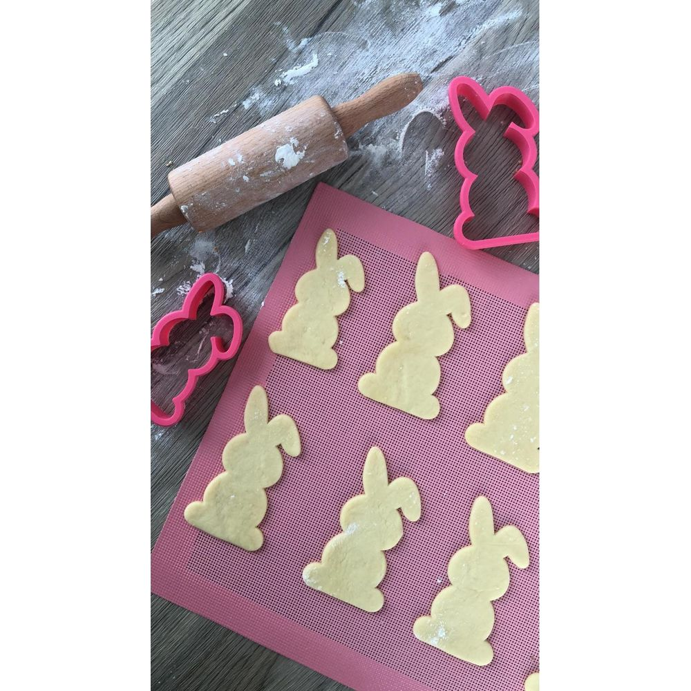 Emporte-pièces lapin et lapins en pâte sur un tapis rose avec rouleau.