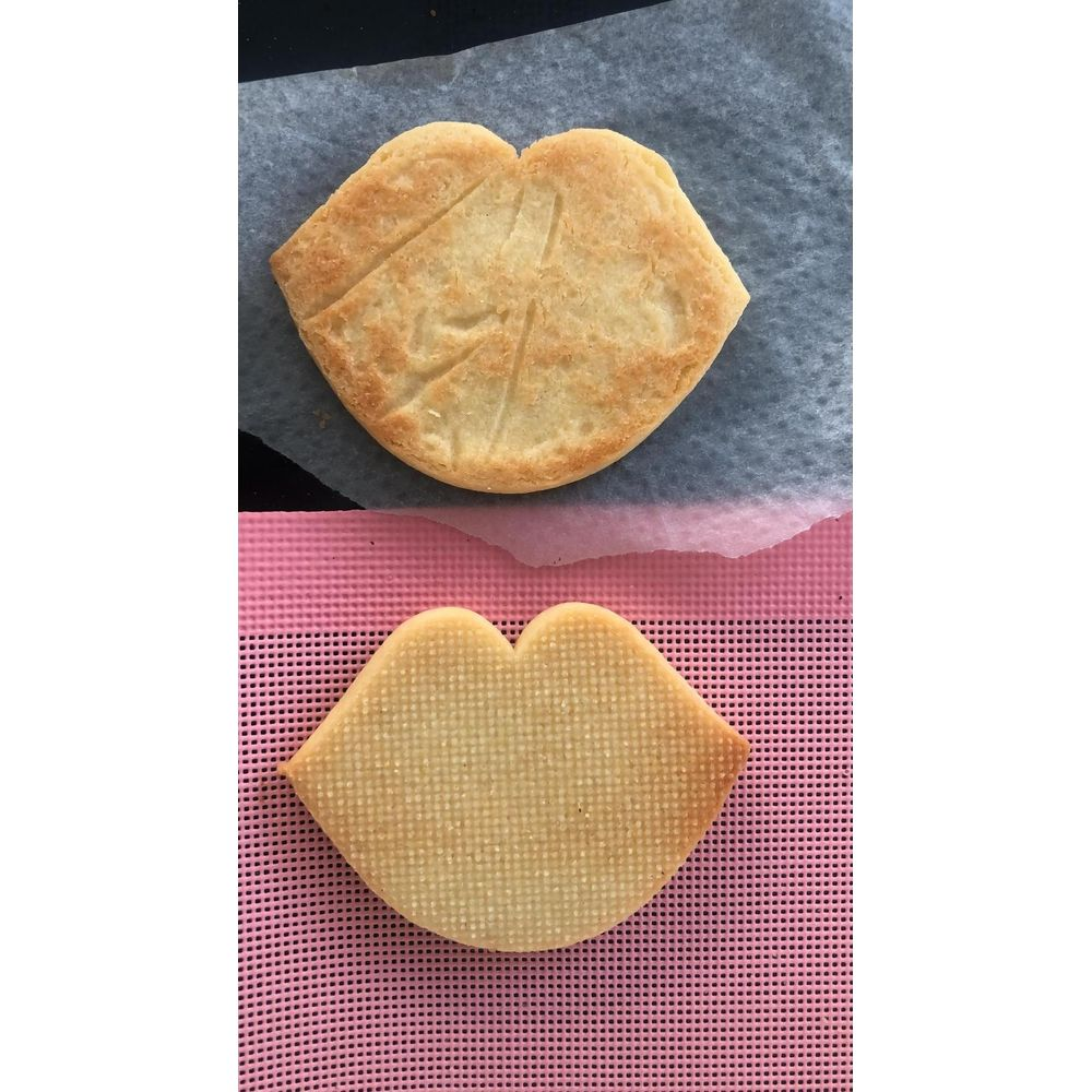 Deux biscuits en forme de lèvres. Le dessus est doré sur papier sulfurisé. Le dessous est plus clair sur tapis rose.