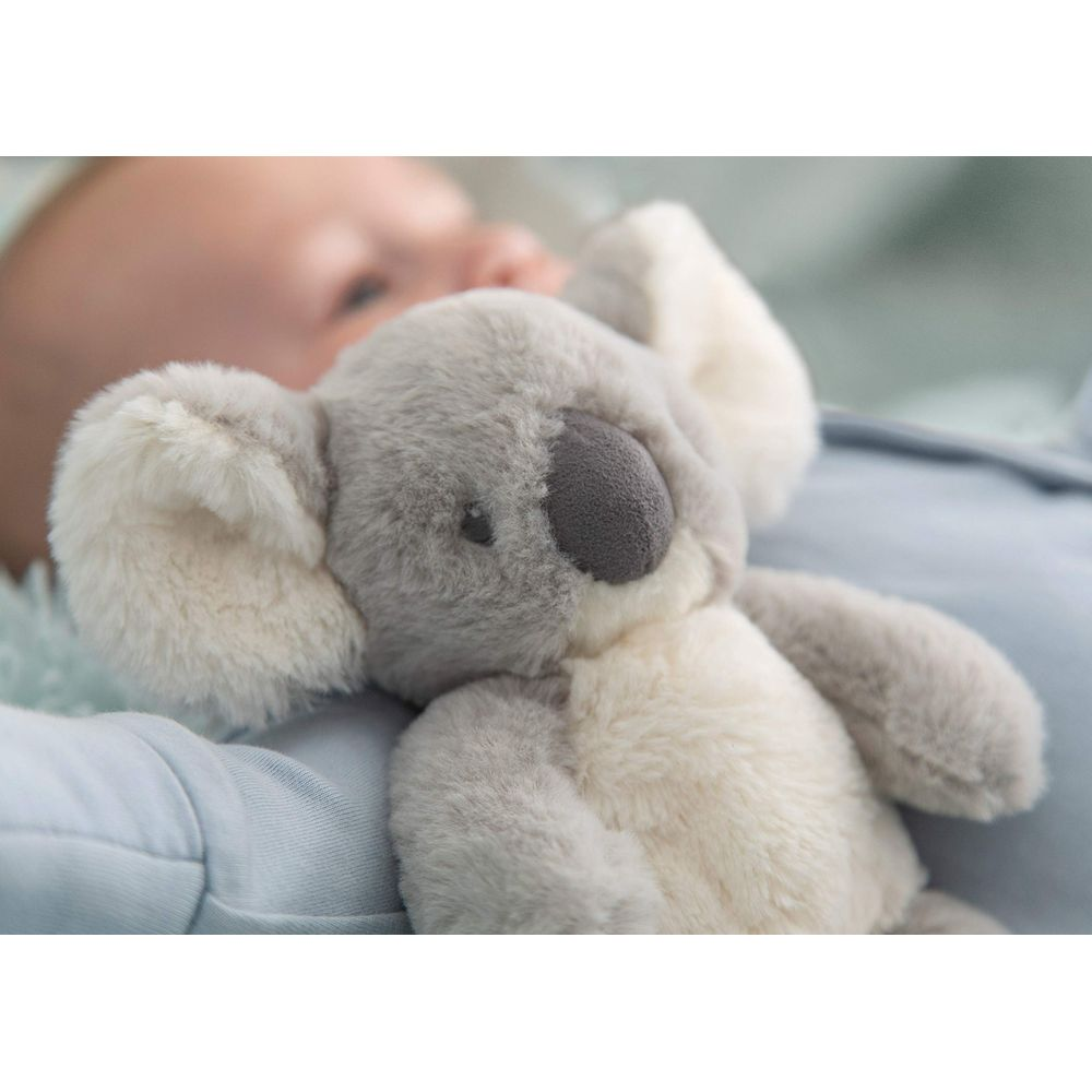 Un peluche di koala grigio giace accanto a un bambino addormentato su un lenzuolo blu.