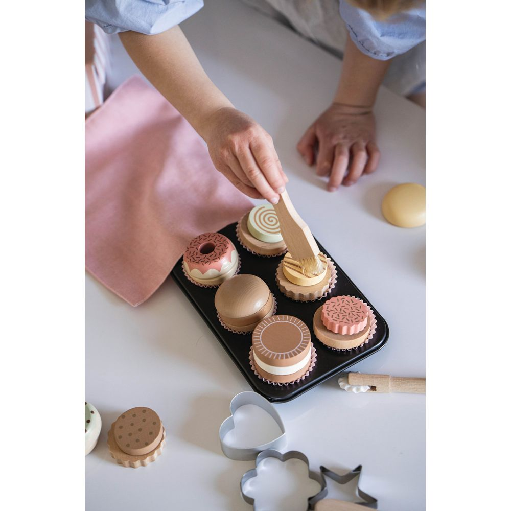 Holz-Gebäck in einer Muffinform, das von einer Hand mit einem Pinsel dekoriert wird.