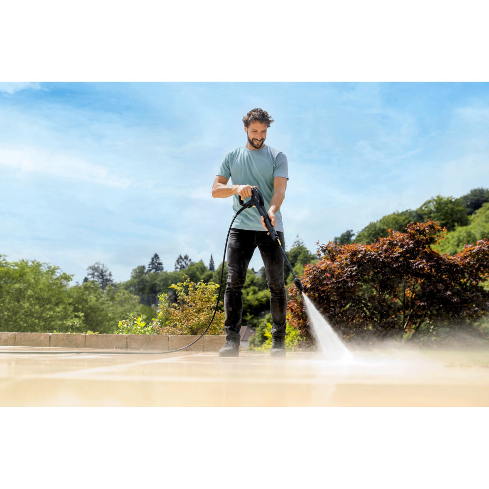 Mężczyzna myje taras myjką ciśnieniową pod błękitnym niebem z drzewami.