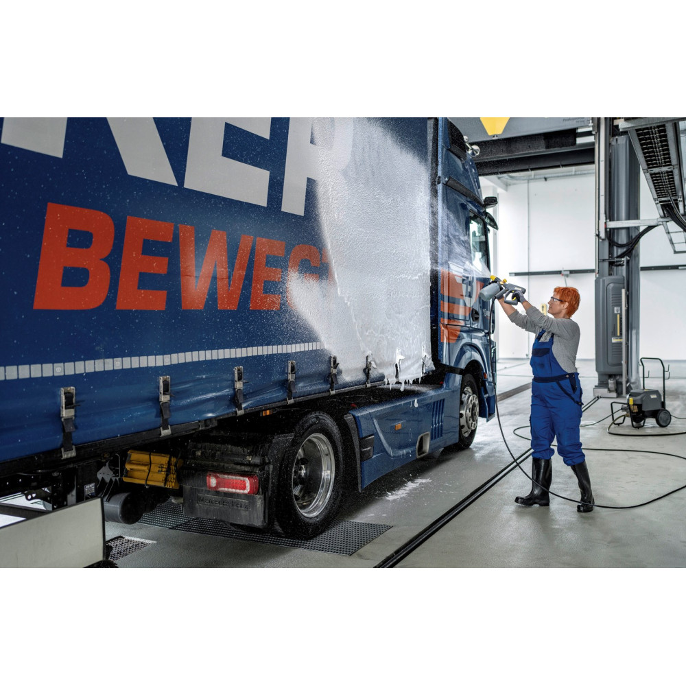 Osoba w niebieskim kombinezonie myje ciężarówkę myjką ciśnieniową.