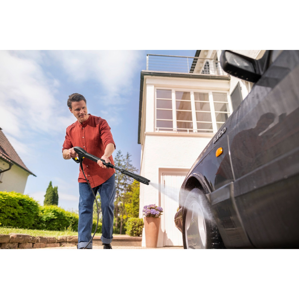 Mężczyzna myje samochód myjką ciśnieniową przed domem.