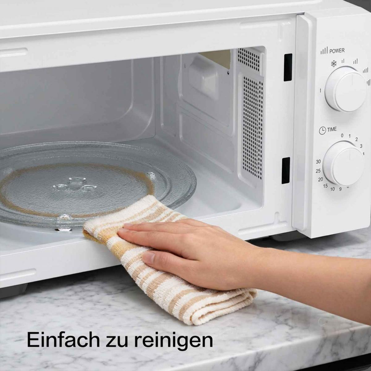 Eine Hand wischt mit einem gestreiften Tuch das Innere einer Mikrowelle aus.