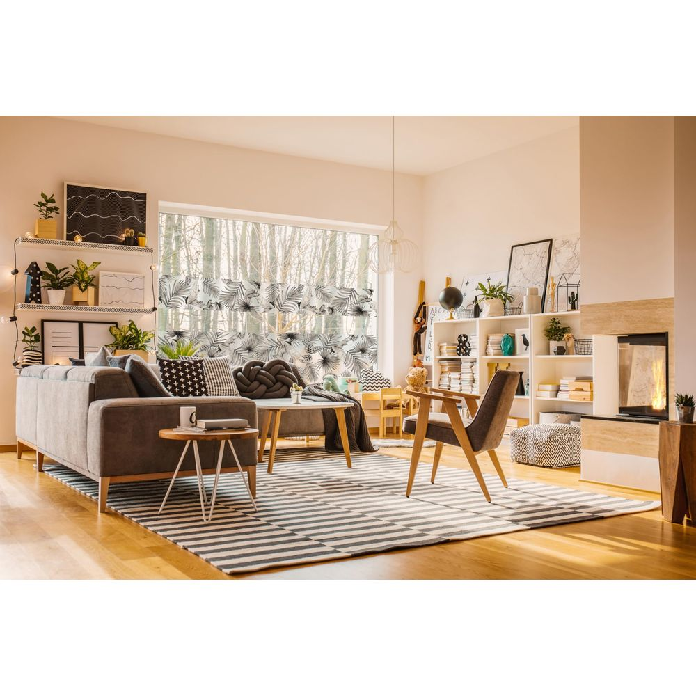 Ein Wohnzimmer mit Sofa, Sesseln, Kamin und Fenster mit Blattmuster.