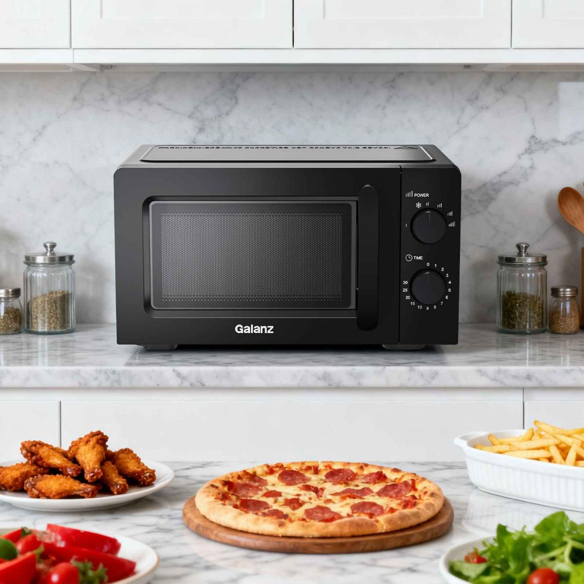 Schwarze Mikrowelle auf Marmorarbeitsplatte mit Pizza, Pommes und Hühnerflügeln.