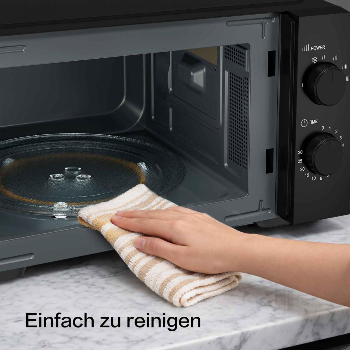 Eine Hand reinigt das Innere einer Mikrowelle mit einem gestreiften Tuch.