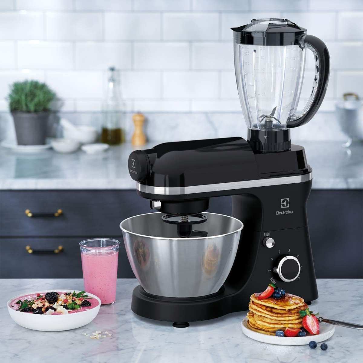 Impastatrice nera con accessorio frullatore, accanto a un frullato e pancake.