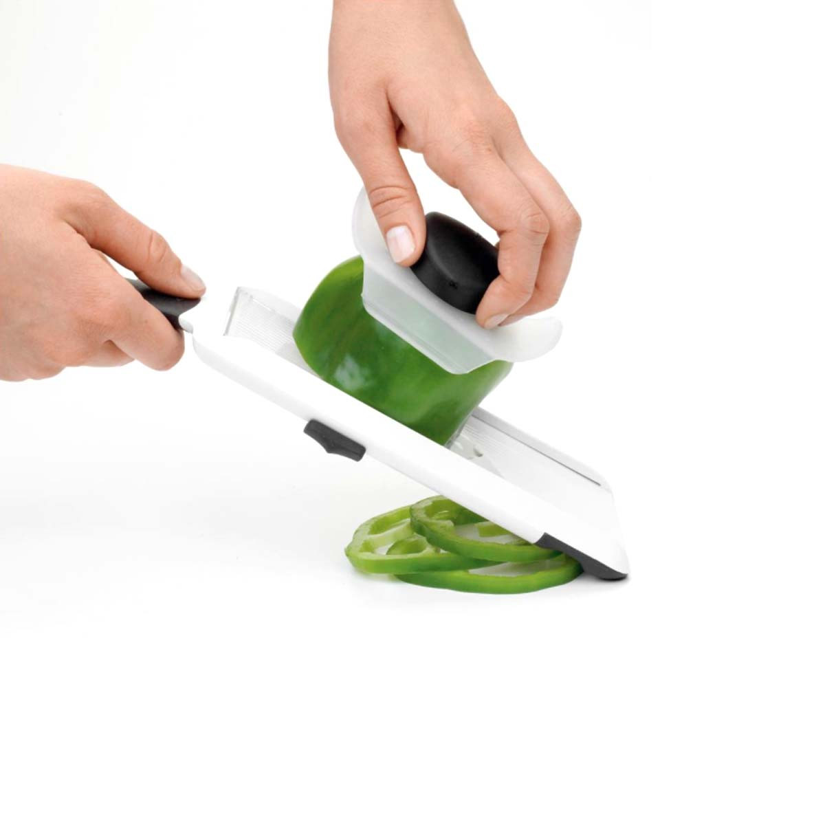 Un peperone verde viene affettato su un mandolino bianco, con fette sotto.