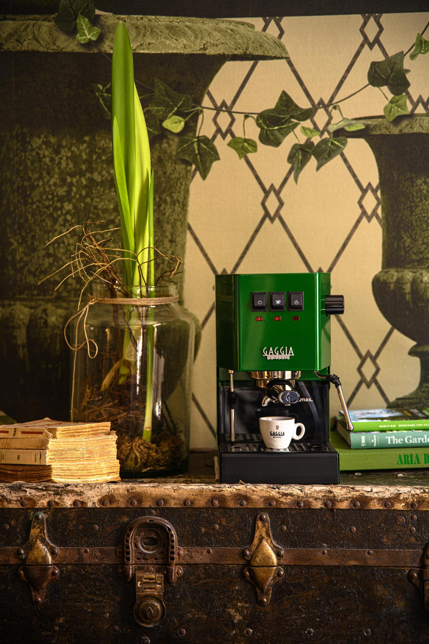 Groene espressomachine met kopje op oude kist, naast boeken en plant.