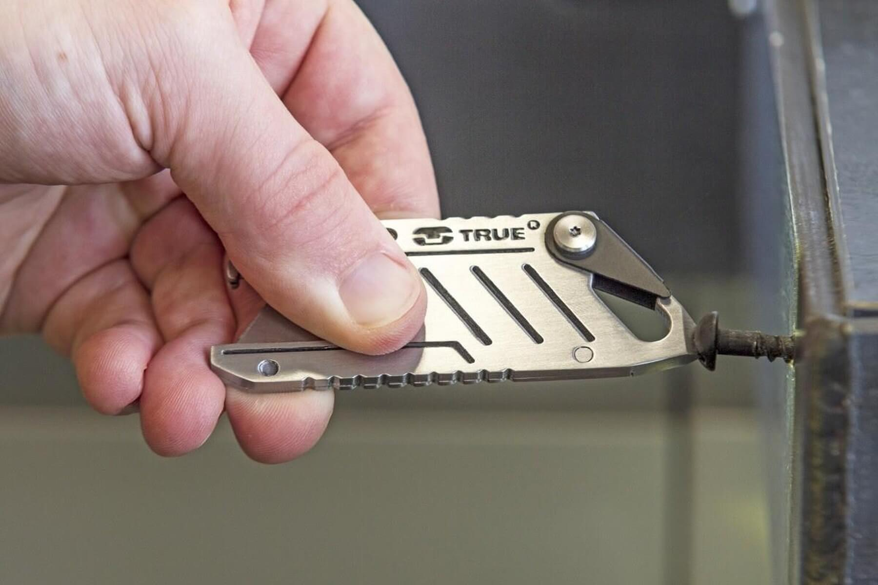 Une main tient un petit outil multifonction en métal pour tourner une vis sur une surface métallique.