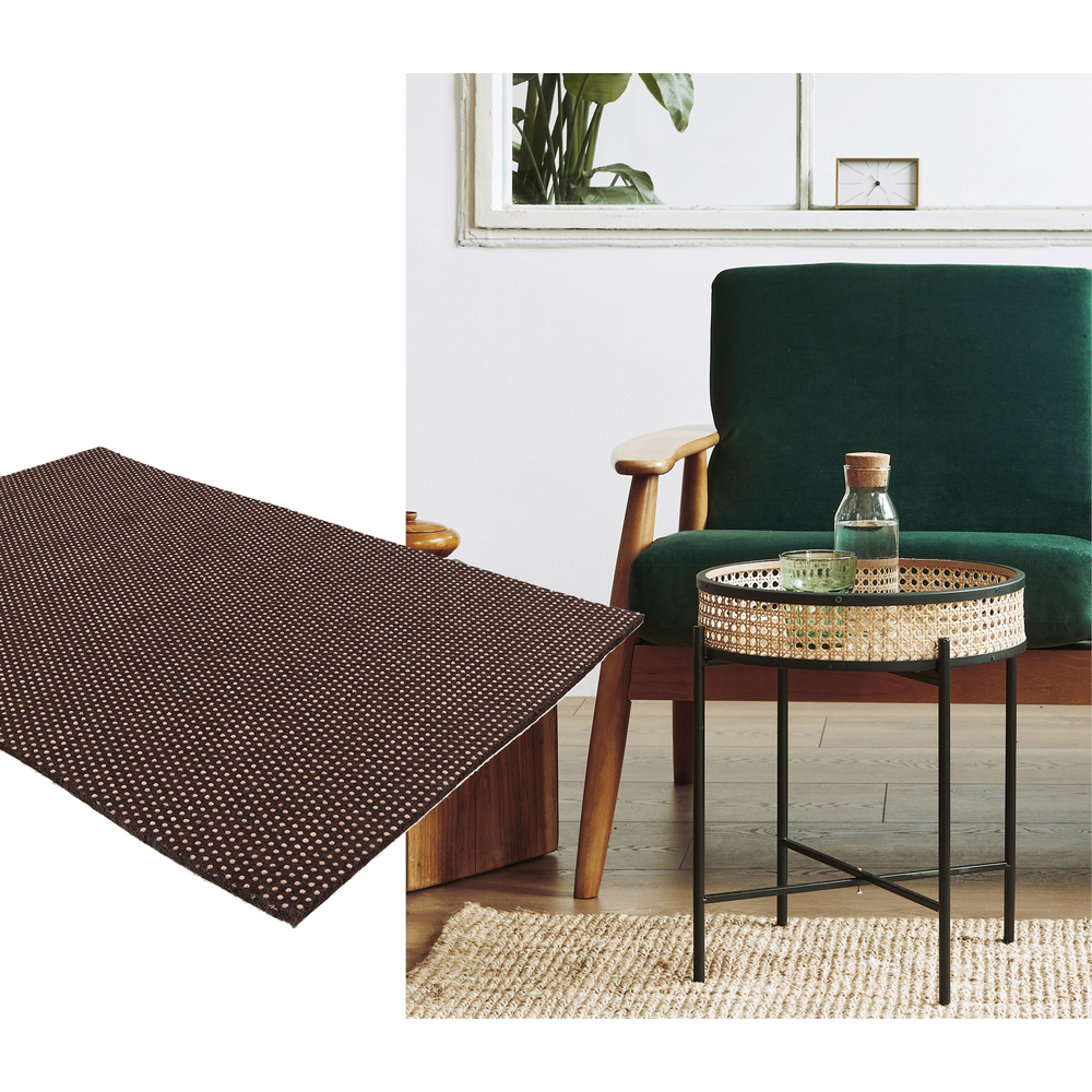 Un tapis marron foncé à pois blancs repose sur un plancher en bois à côté d'une chaise verte.