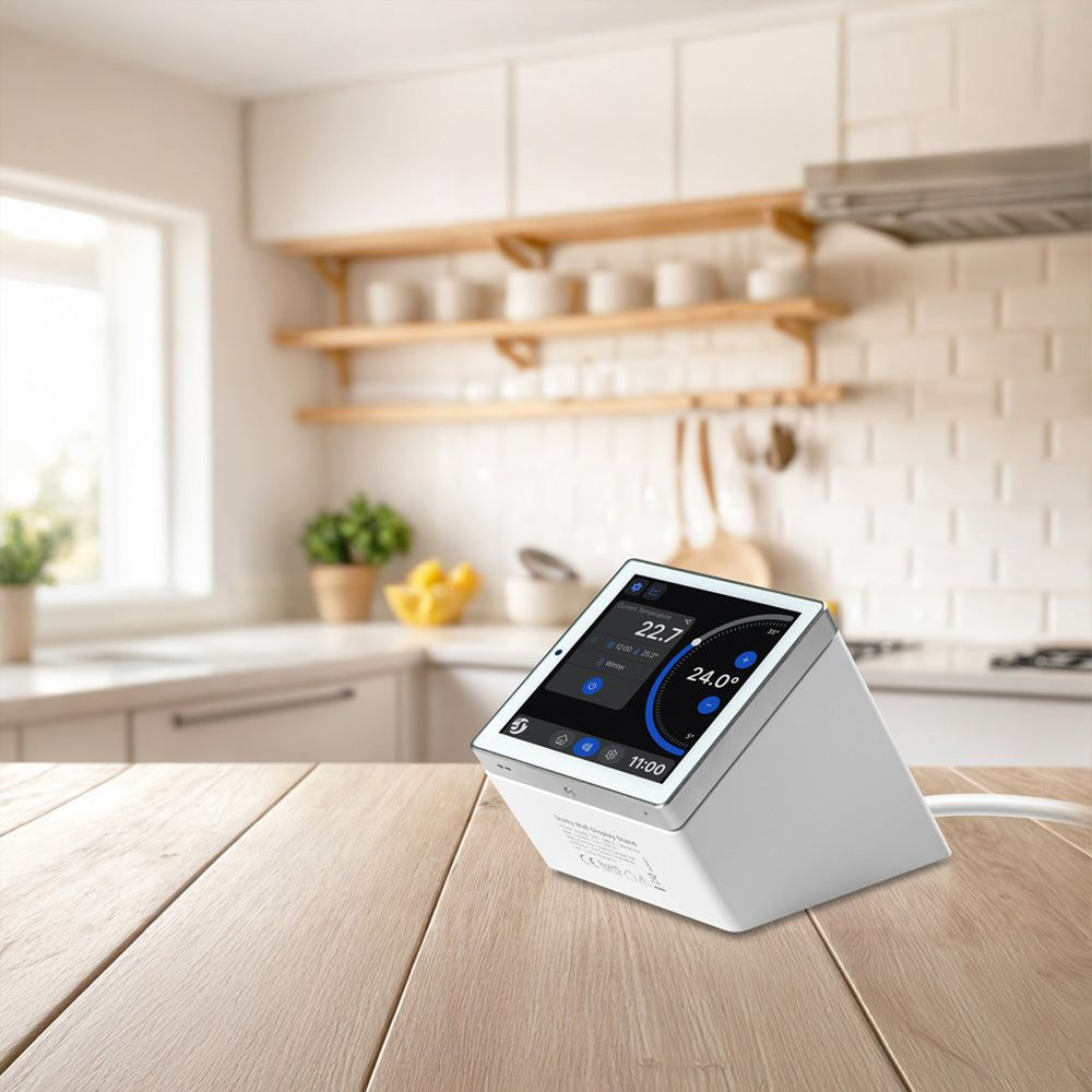 Un thermostat numérique blanc avec écran affichant la température est sur une table en bois dans une cuisine.