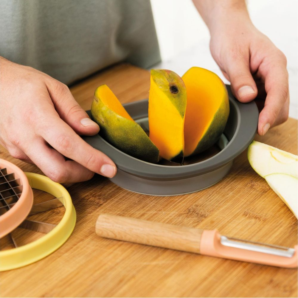 Mani che usano affetta mango su tagliere di legno. Pelapatate nelle vicinanze.
