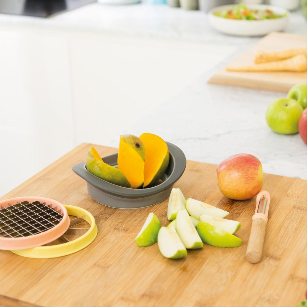 Affettatrici per mango e mele su un tagliere di legno con frutta tagliata.