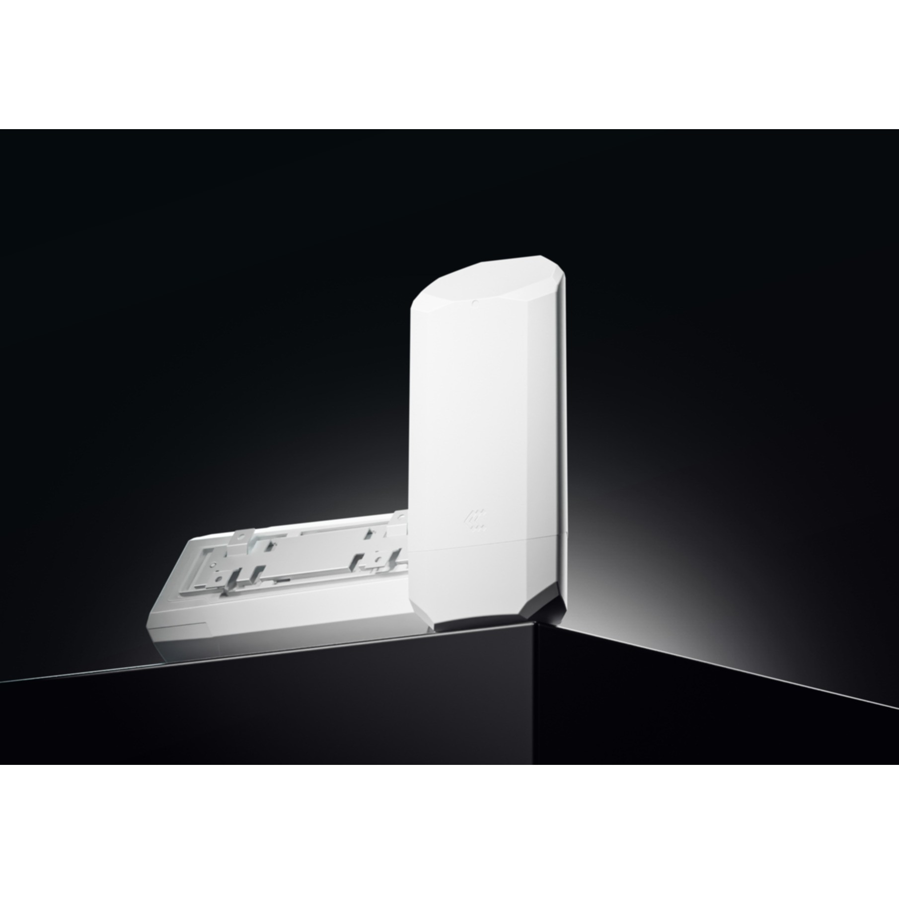 Un appareil blanc et rectangulaire se dresse sur une surface noire à côté d'un support.