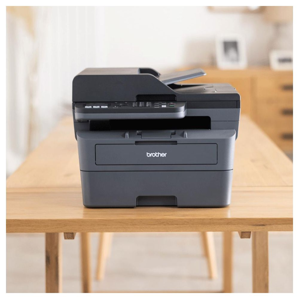 Ein grauer Brother Drucker steht auf einem Holztisch. Der Drucker hat einen Scanner oben.
