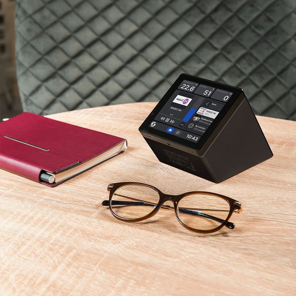 Sveglia digitale con touchscreen, taccuino e occhiali su un tavolo di legno.