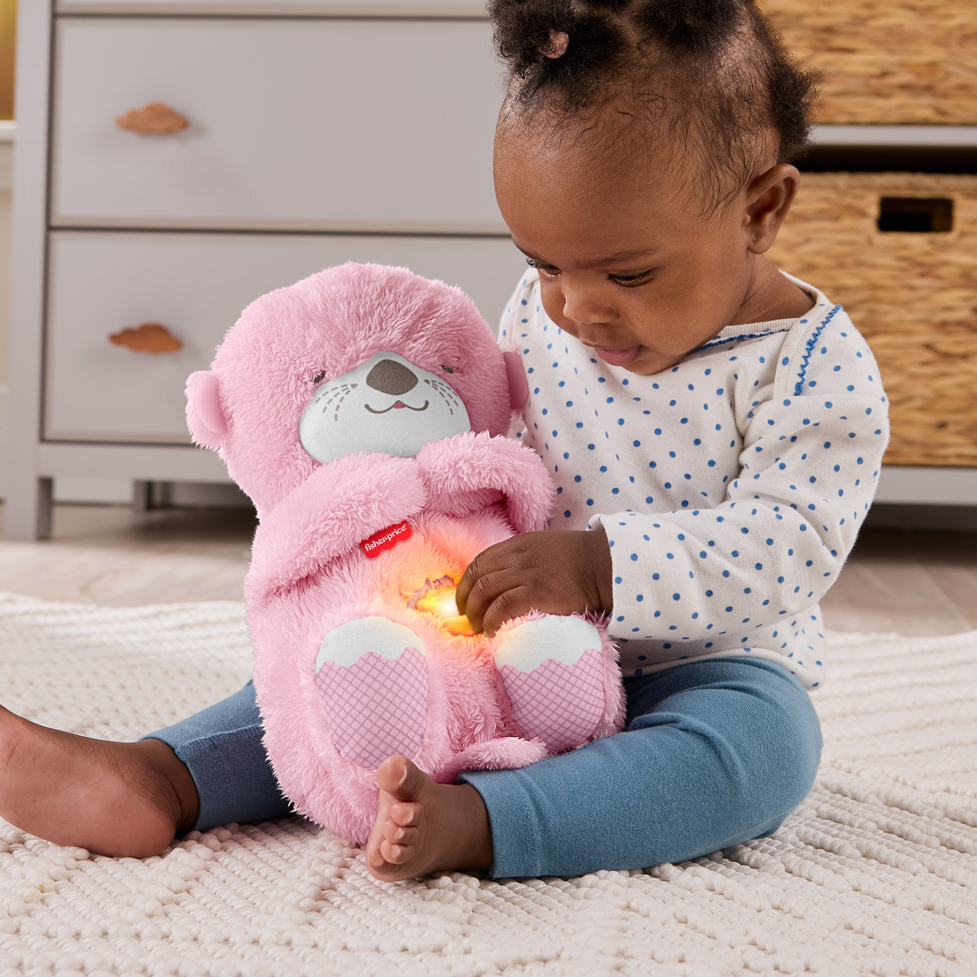 Ein Baby hält einen leuchtenden rosa Otter, der auf einem Teppich sitzt.