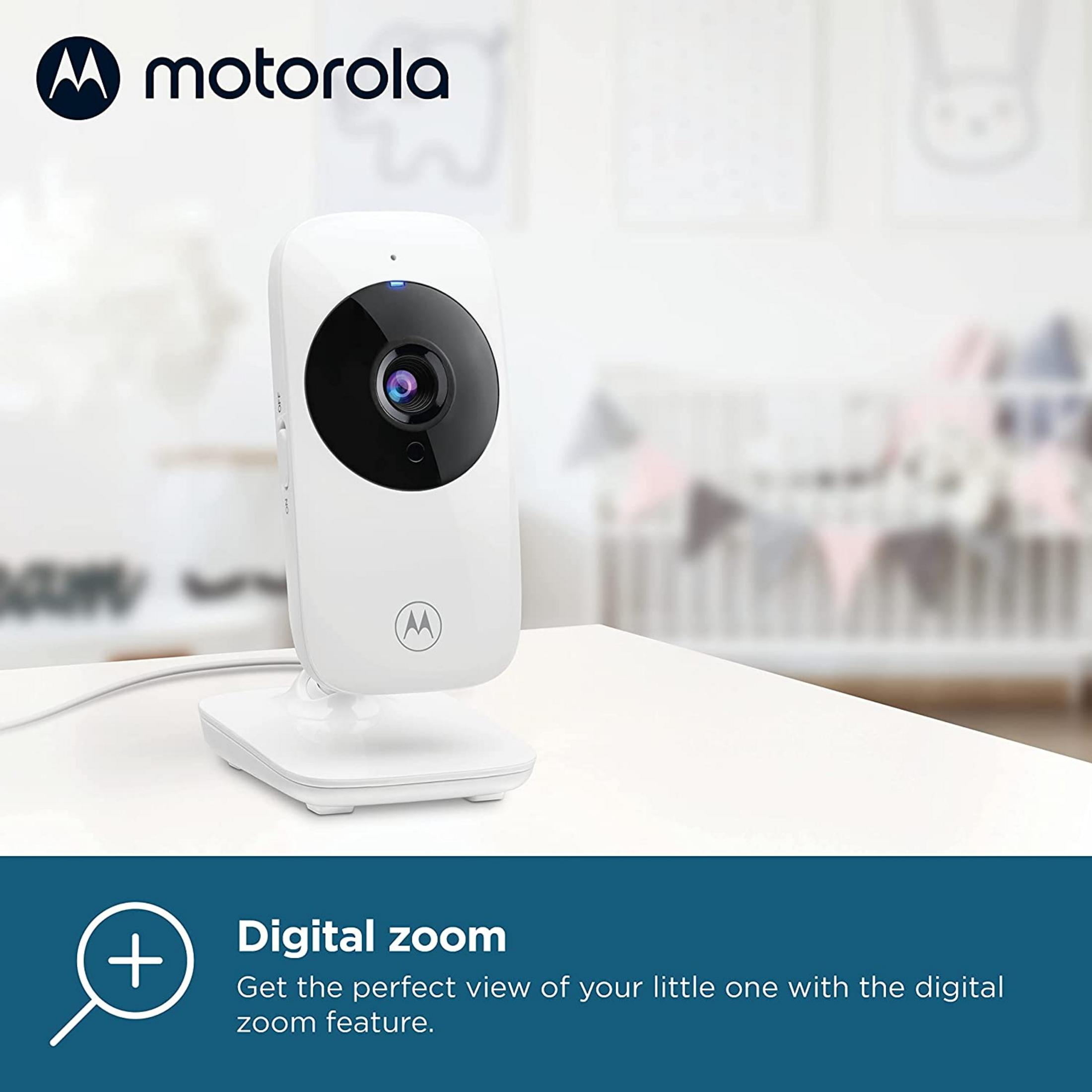 A white Motorola baby monitor on a table in front of a crib.
