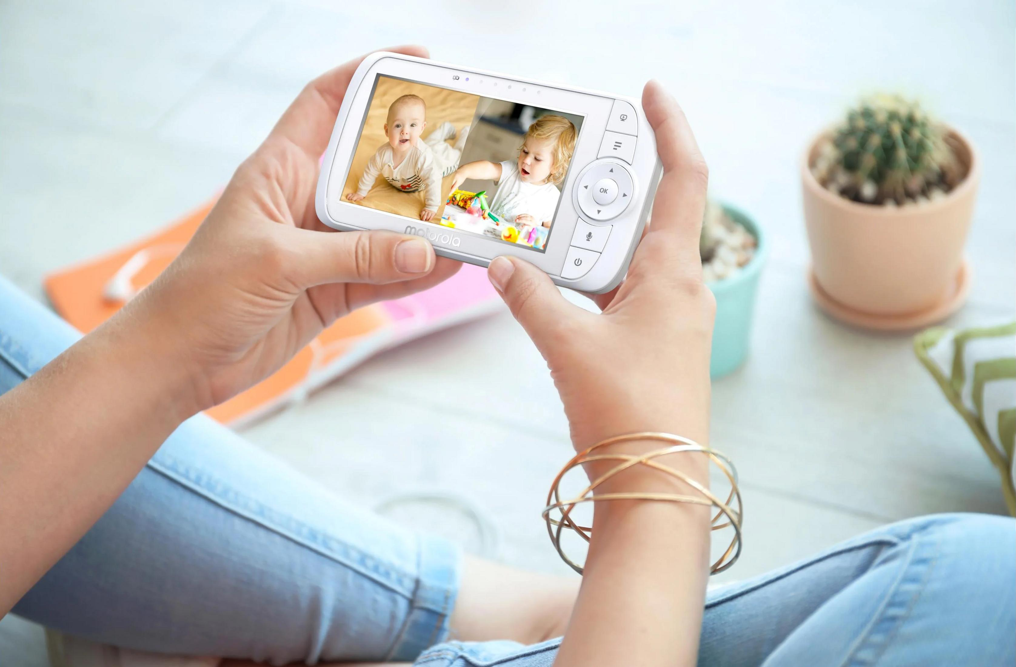 Hands holding a baby monitor showing two babies on screen.