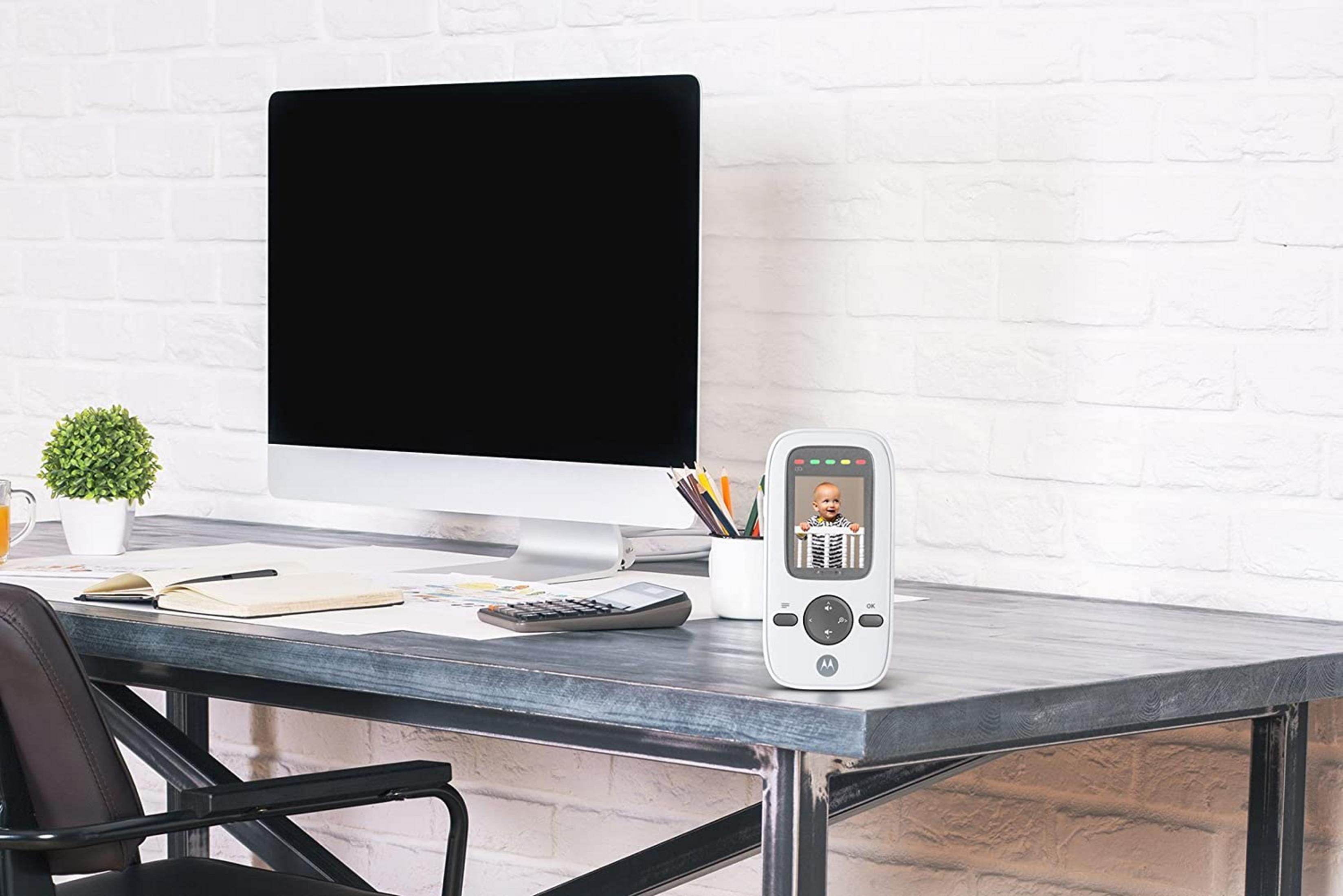 Ein Schreibtisch mit einem Monitor, einem Babyphone, das ein Baby zeigt, und Büromaterial.