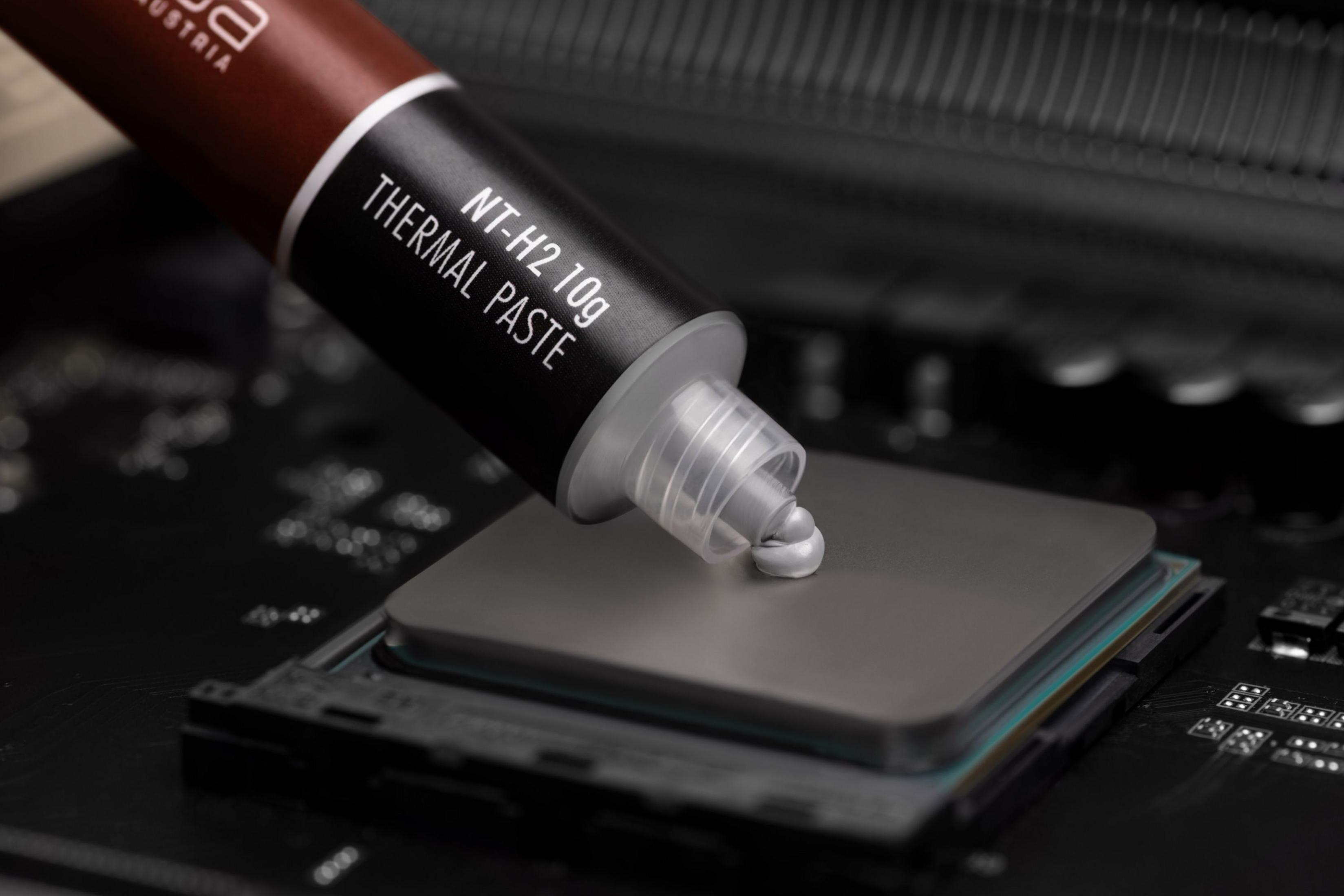 Eine Tube Wärmeleitpaste trägt graue Paste auf einen Computerprozessor auf einer Platine auf.